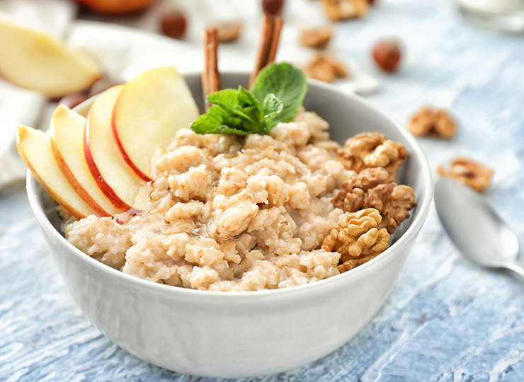 Tasty oatmeal with apple and walnut in bowl on table