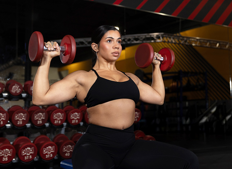 Woman holding dumbbells at shoulder height in the gym.